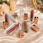 Miss Rose Lip Void liquid lip gloss collection of 6 shades in rose gold bottles open with applicators on cream satin fabric with white roses and gold mirror in romantic bridal flat lay