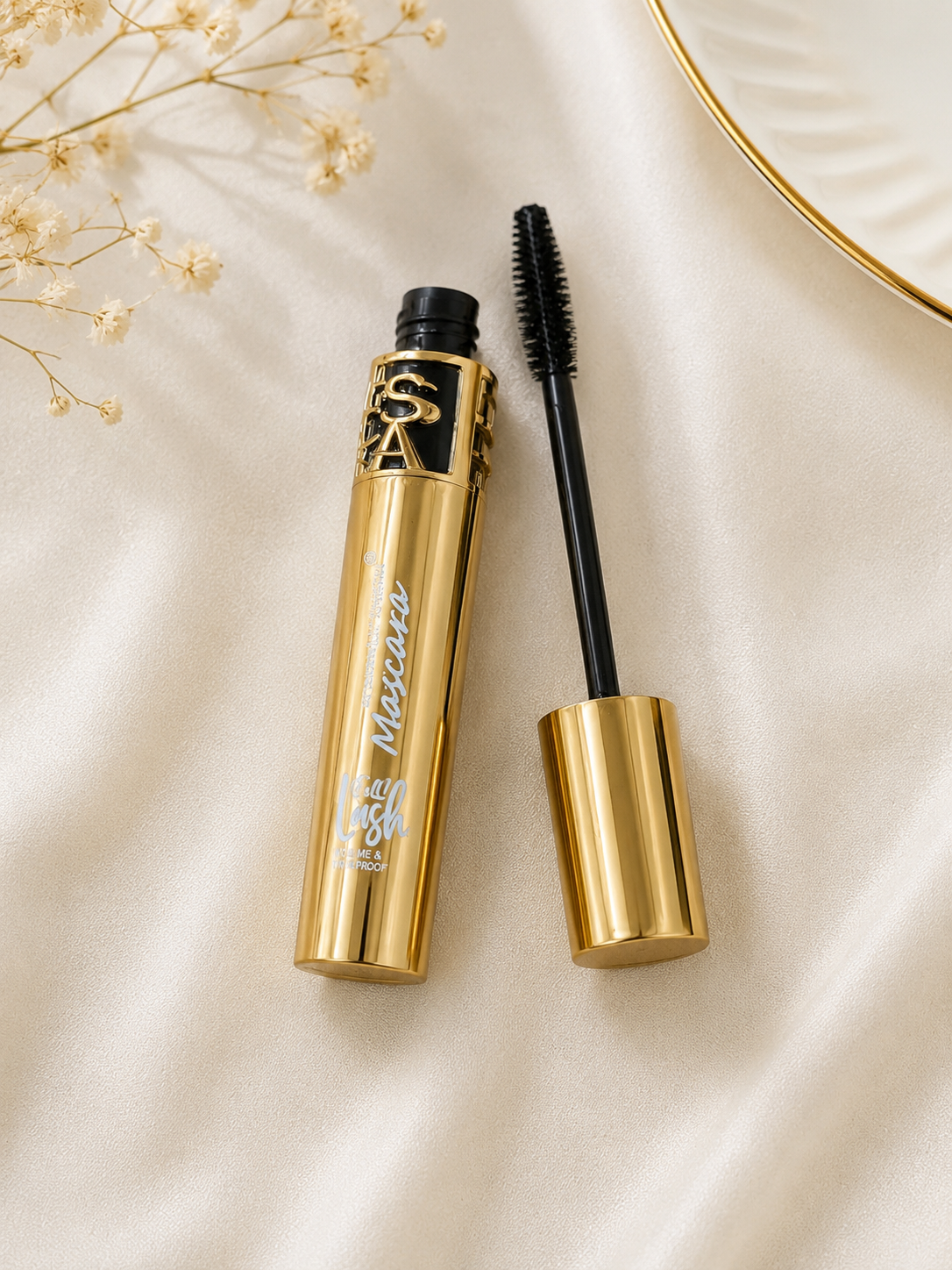HSA luxury gold mascara tube open with black volumising wand applicator on cream satin fabric with dried flowers